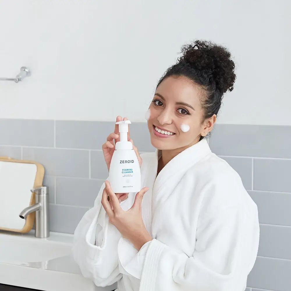 Femme tenant un flacon blanc ZEROID Foaming Cleanser. Texte: Foaming Cleanser, mild care for sensitive & dry skin. 240ml/8.12 fl oz.