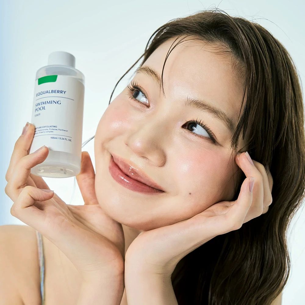 Vrouw houdt een tonerfles vast. Productetiket zichtbaar. Lichtblauwe achtergrond.