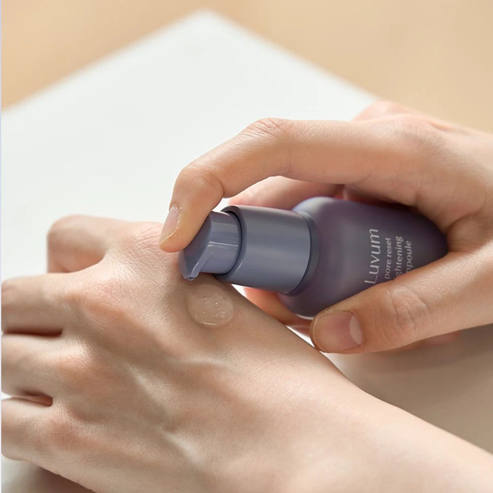 Handen houden een paarse fles vast. Een serum wordt op de handpalm aangebracht. Op de fles staat "Luvum pore reset tightening ampoule".