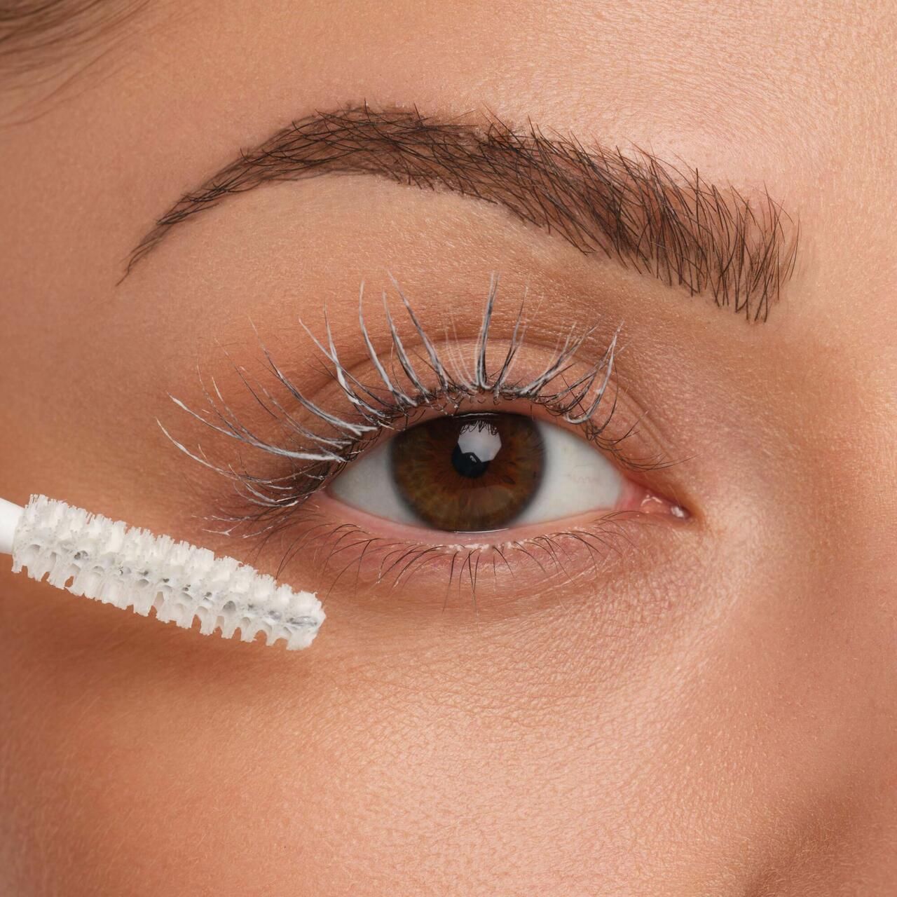 Oog met wimpers bedekt met witte mascara basis. Borstel in de buurt van het oog.