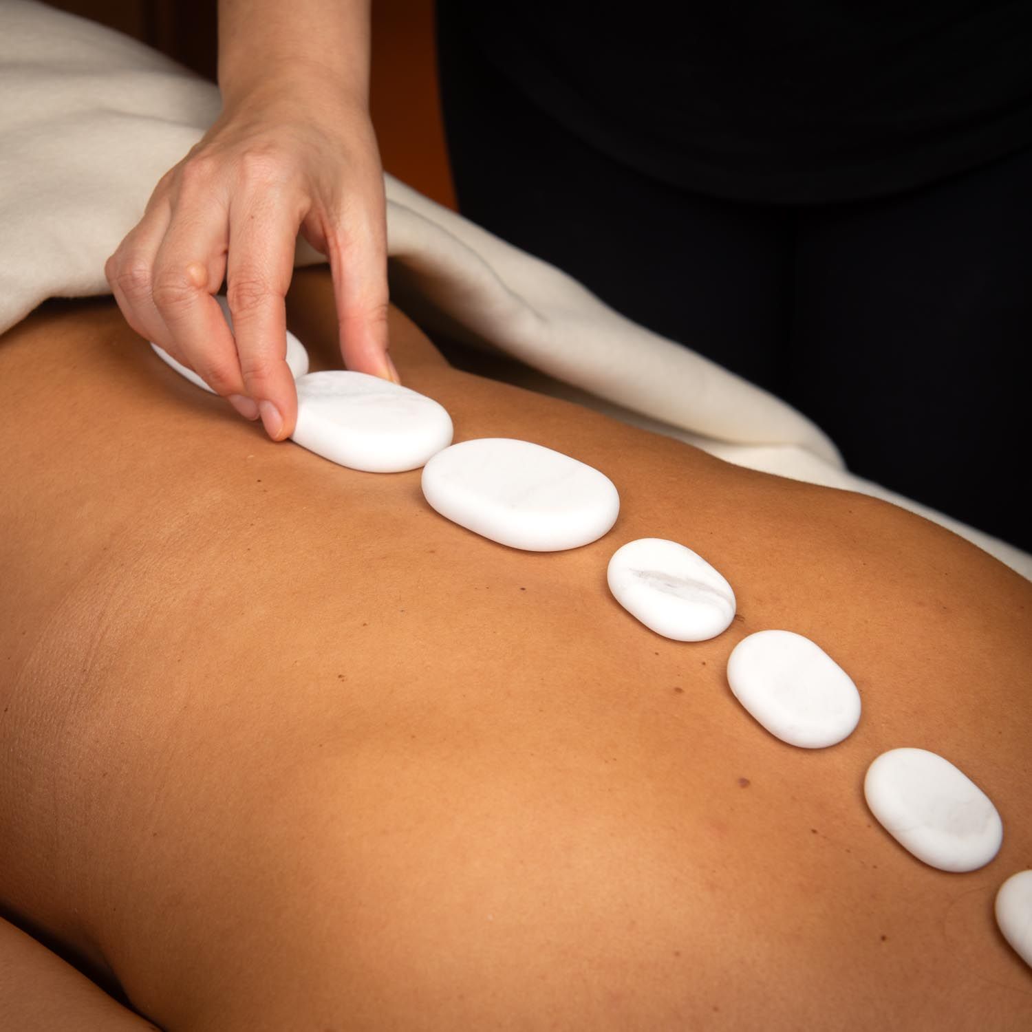 Personne place des pierres blanches ovales sur le dos d'une autre. Sur une table de massage.