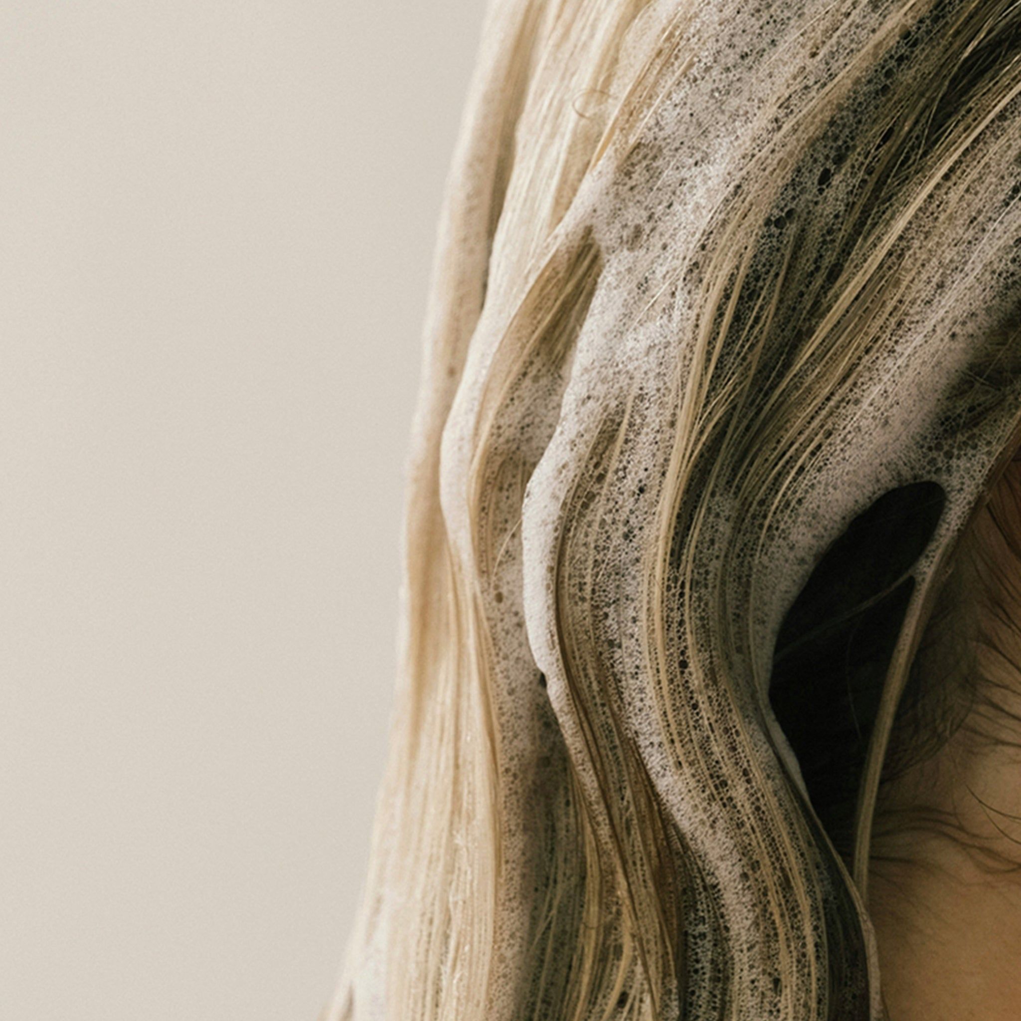 Cheveux blonds recouverts de mousse. Gros plan, peau claire en arrière-plan.
