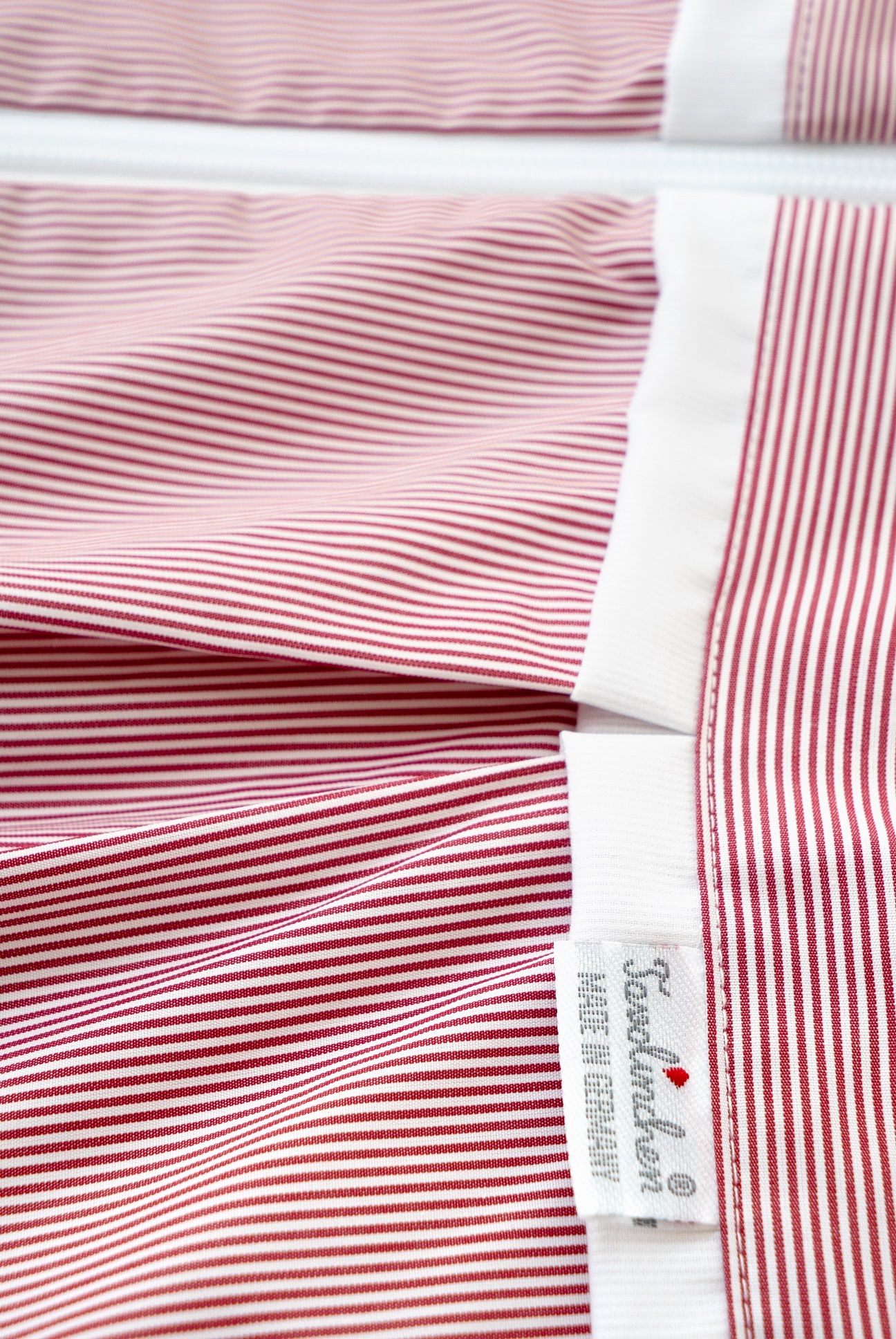 Vue détaillée de la gigoteuse. Rayures rouges et blanches, ourlet blanc. Marque Tavolinchen, Made in Germany.