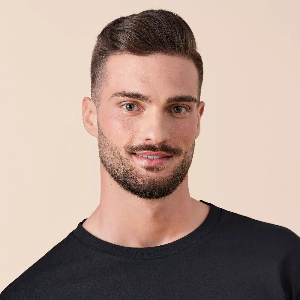 Portret van een man met baard en donker t-shirt. Lichtbruine achtergrond.