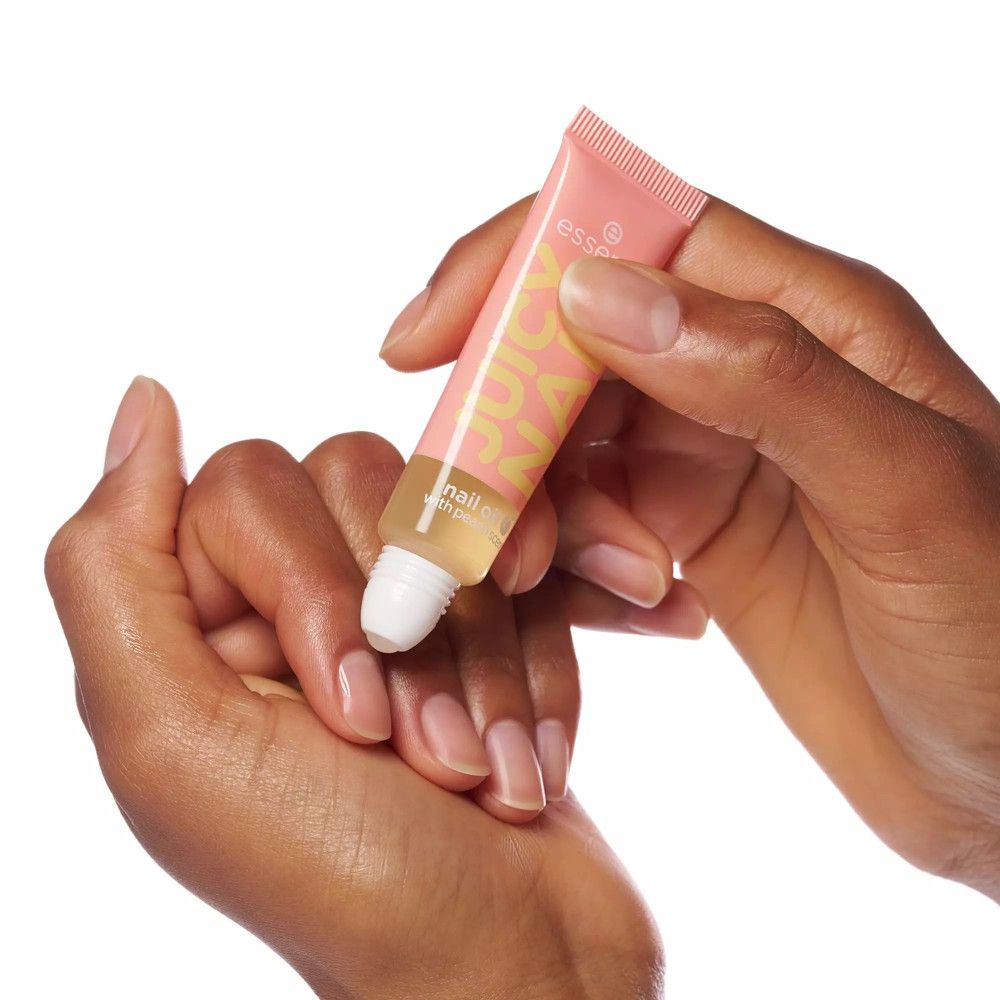 Mains tenant un tube d'huile pour ongles. Tube rose avec texte jaune JUICY NAIL. Marque : essence. Produit appliqué sur les ongles.