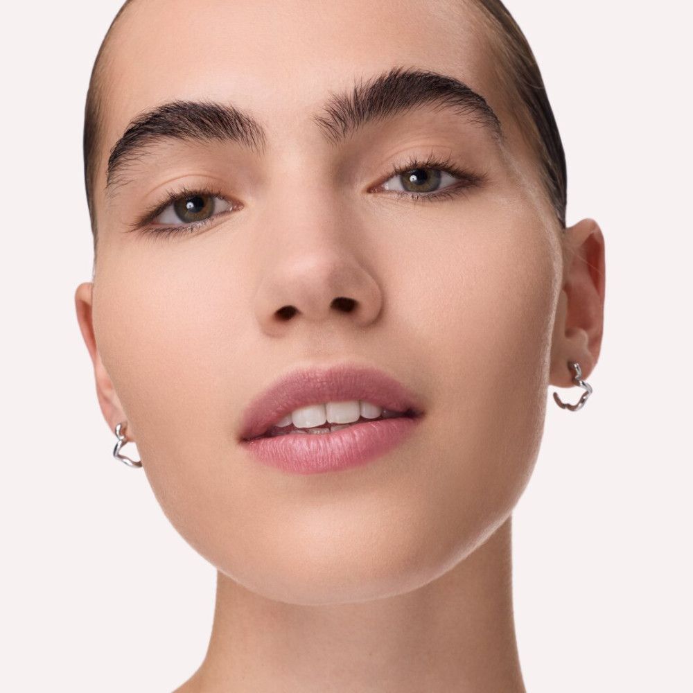 Gros plan d'un visage. La personne a la peau claire, des sourcils foncés et porte des boucles d'oreilles. Les lèvres sont légèrement maquillées.