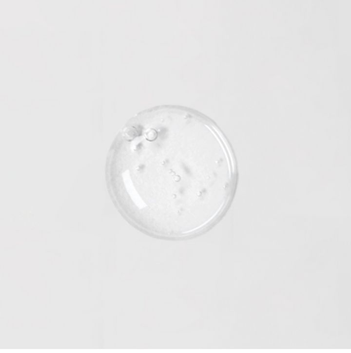 Heldere, ronde serumdruppel op witte achtergrond. Kleine belletjes zichtbaar.