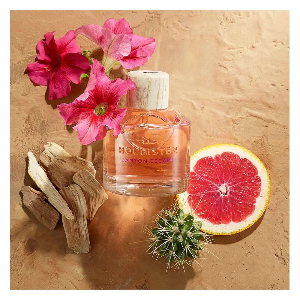 Fles Hollister Canyon Escape Eau de Parfum Spray met houten dop. Omringd door bloemen, stukken hout, grapefruit en cactus.