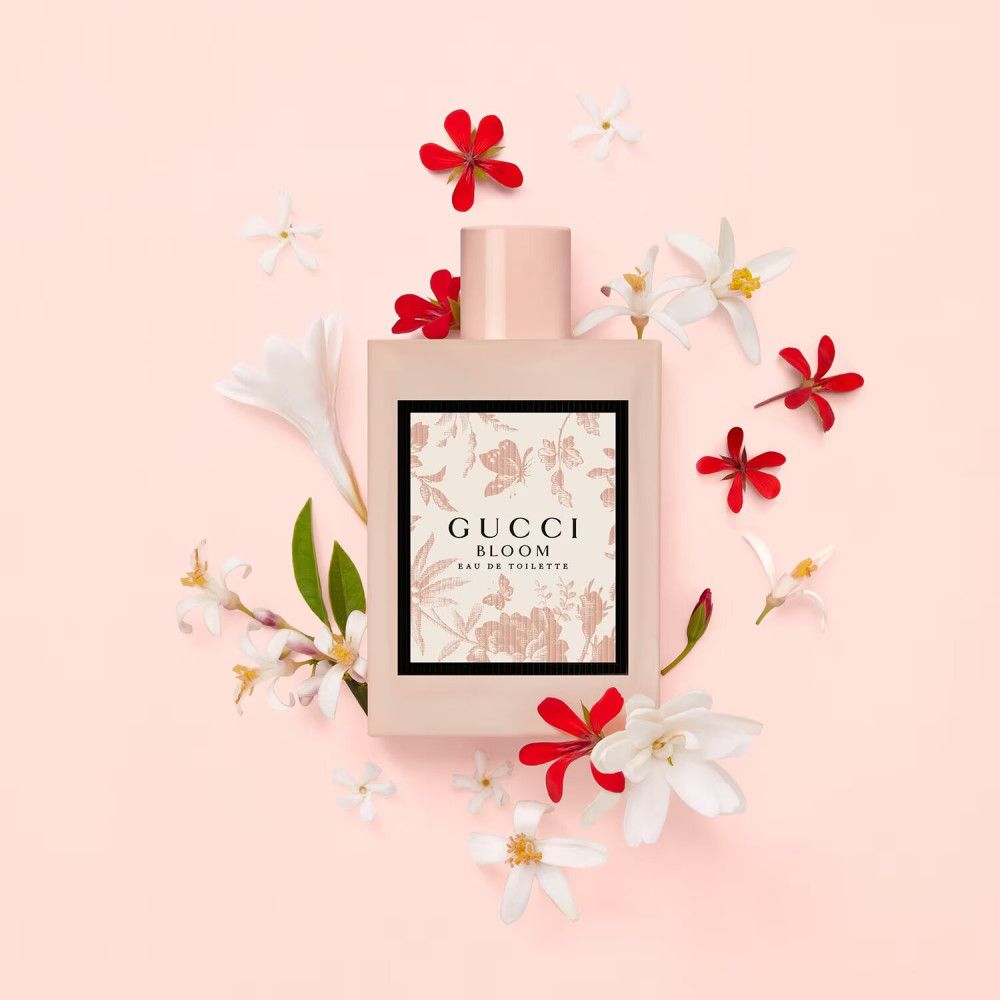Roze fles met bloemenprint, omringd door bloemen. Opschrift: Gucci Bloom Eau de Toilette.