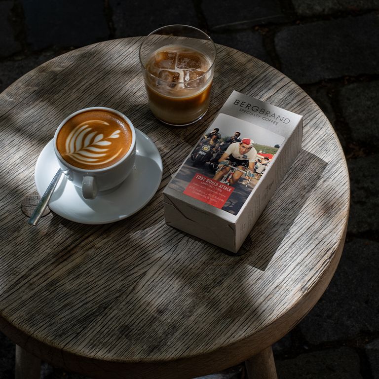 Koffiekopje met latte art, koffieverpakking en drank met ijsblokjes op houten tafel. BERGBRAND Eddy would Attack.