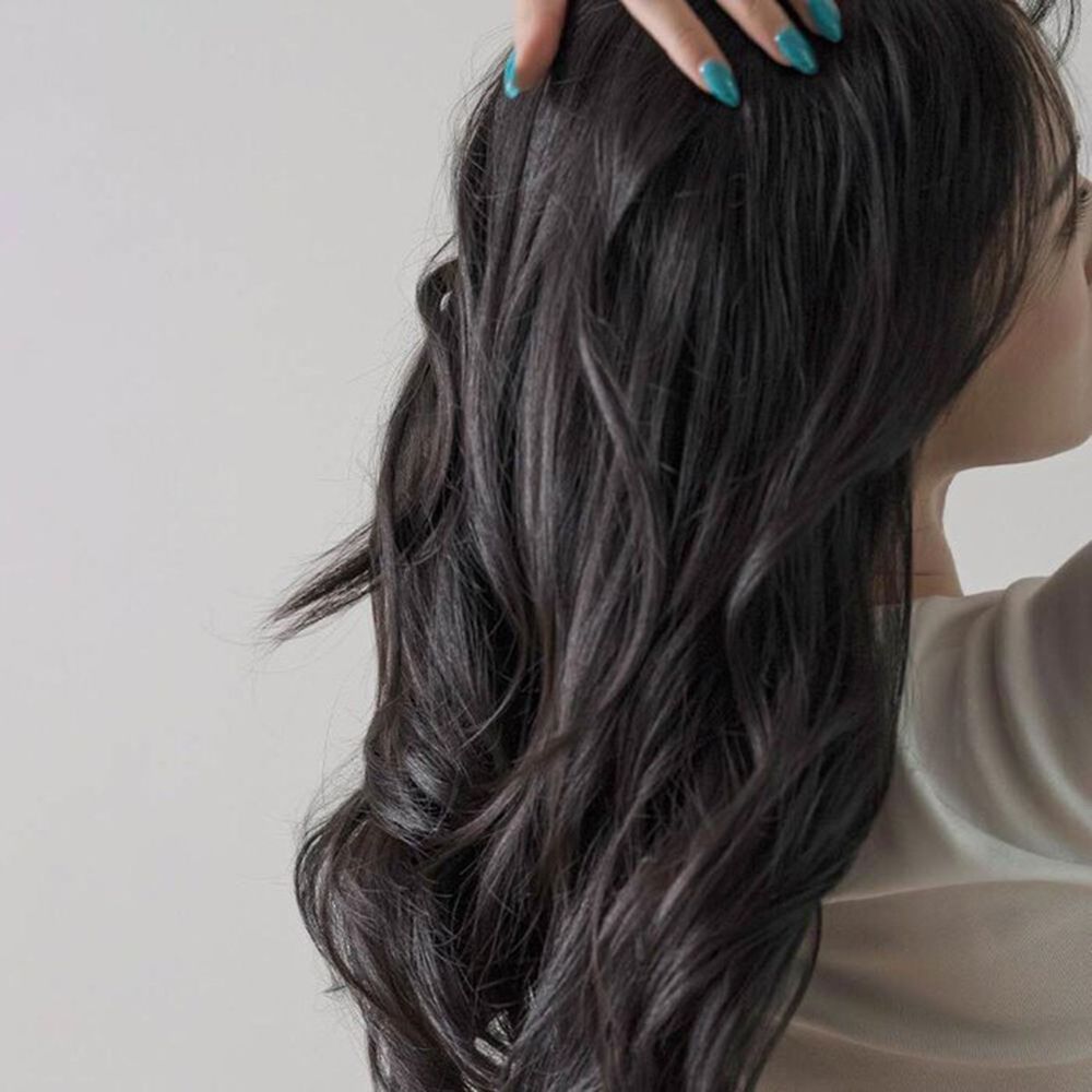 Persoon met donker haar die haar krullende haar aanraakt. Het haar is golvend en valt natuurlijk.