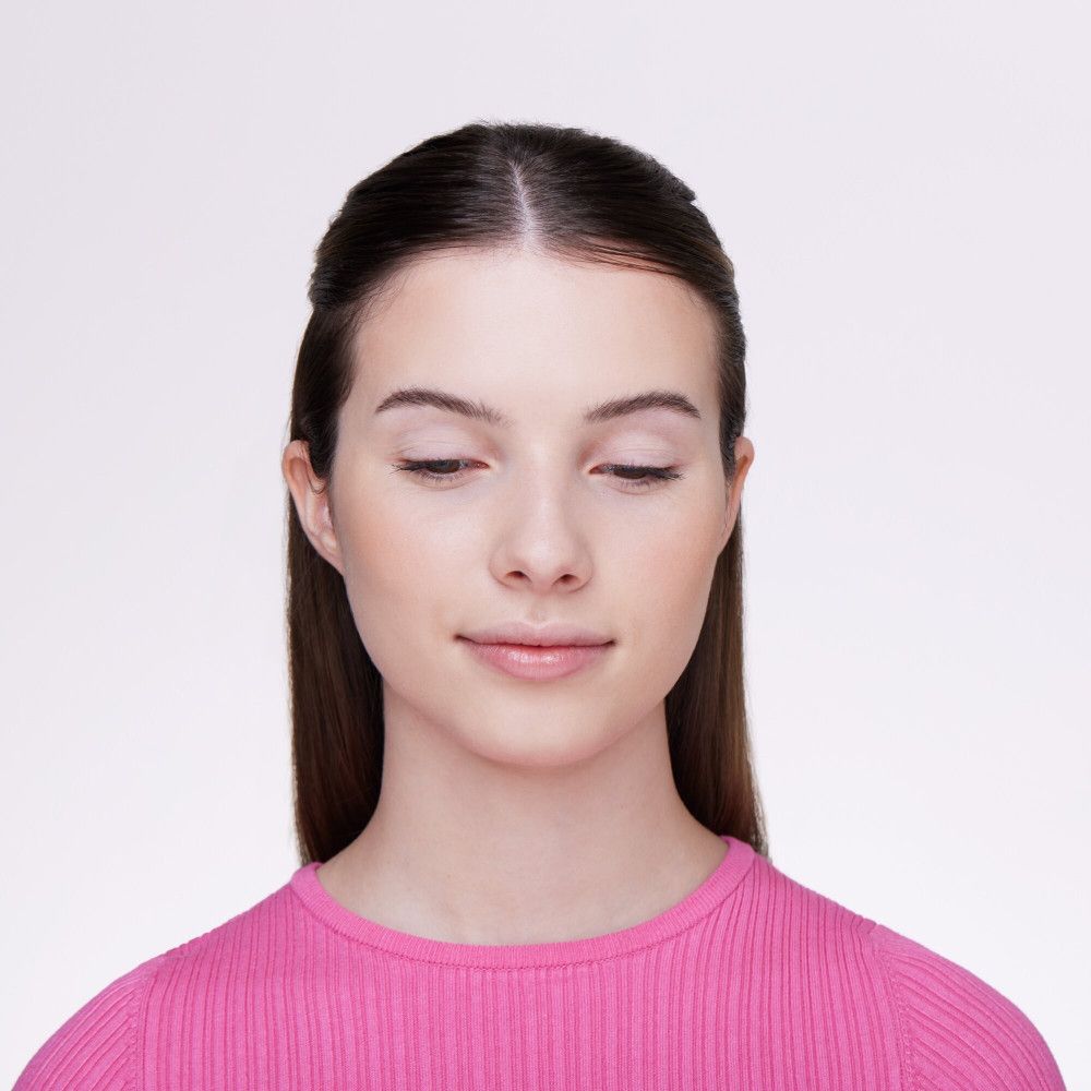 Gros plan d'une femme en haut rose. Elle regarde vers le bas, les lèvres légèrement entrouvertes.