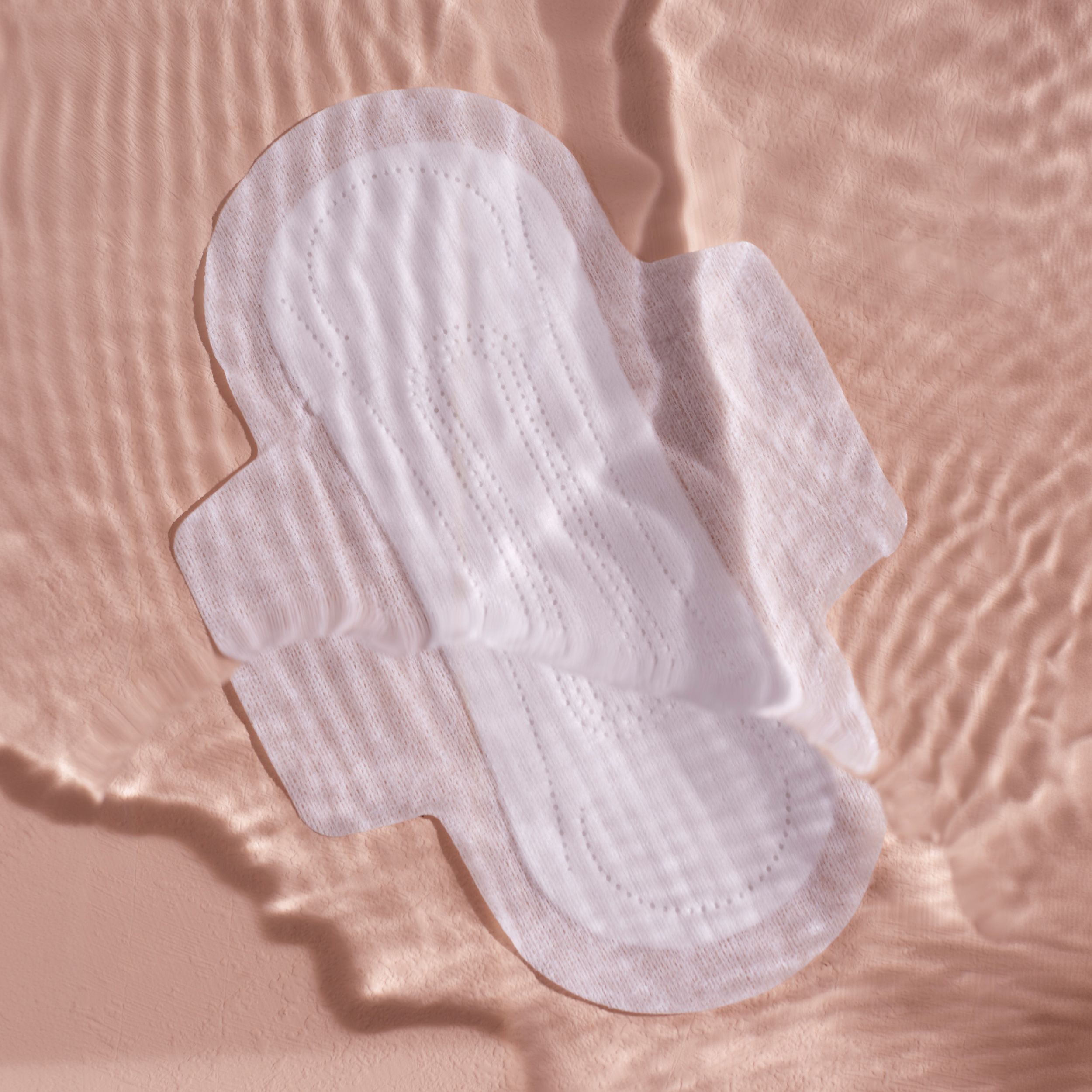 Serviette hygiénique blanche avec ailettes. Sur fond rose. Coutures et structure visibles.