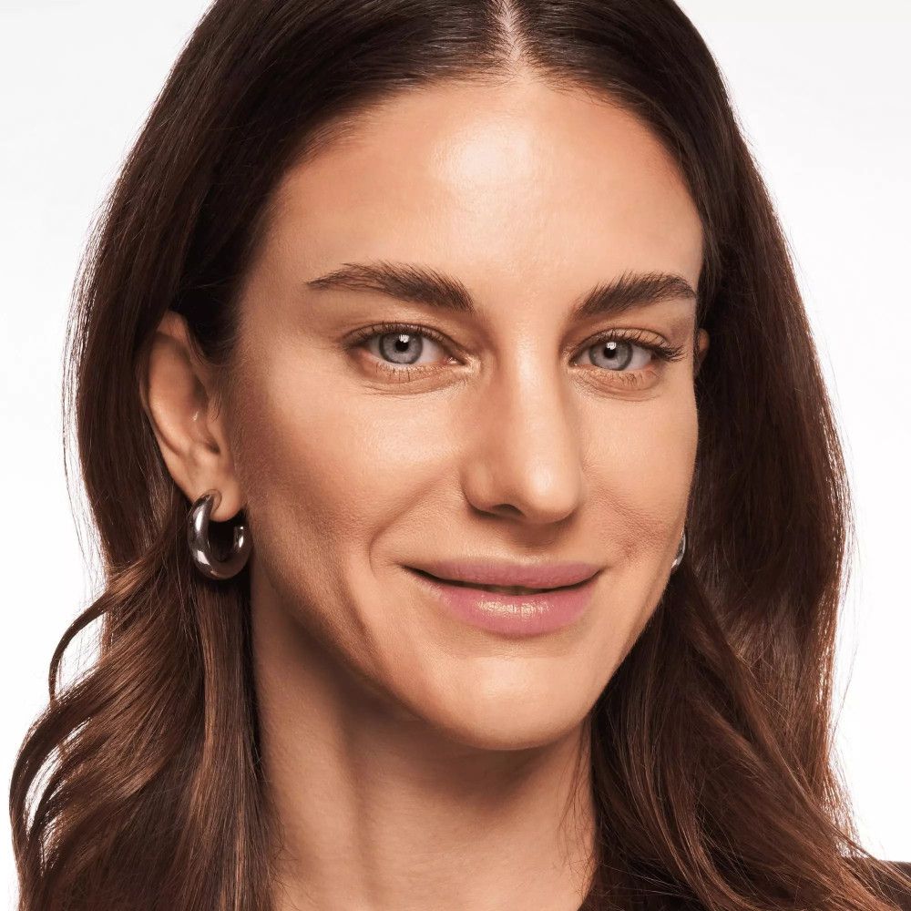 Portret van een vrouw met bruin haar en blauwe ogen. Ze draagt oorbellen.