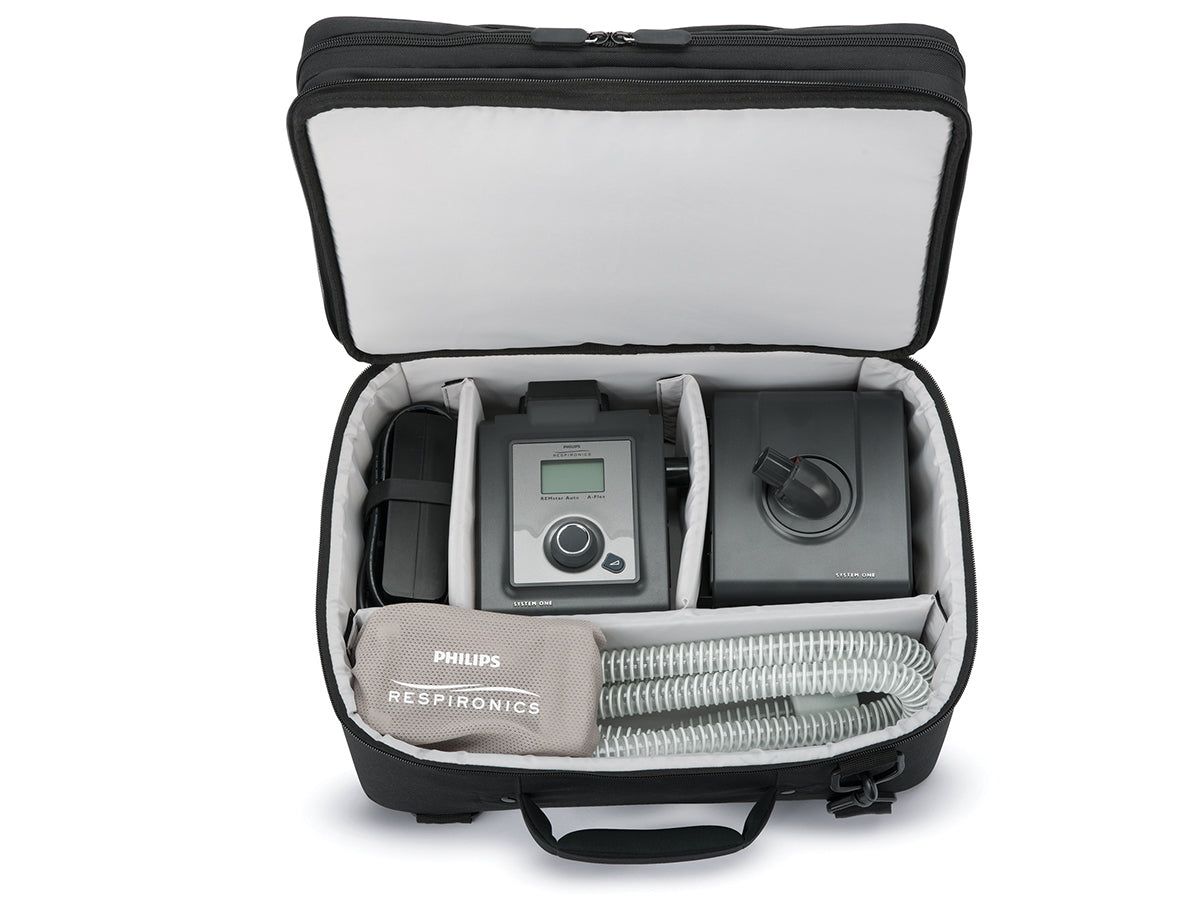 Sac de voyage noir, ouvert, avec appareil thérapeutique Philips Respironics, bloc d'alimentation et tuyau à l'intérieur.