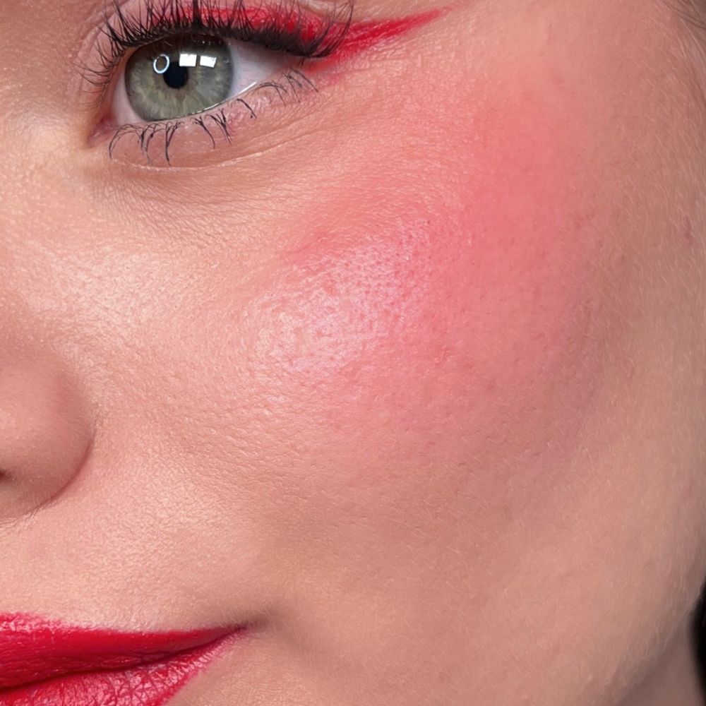 Close-up van een gezicht met rode lippenstift, eyeliner en blush. Groen oog. Product: ALL TIGERS.