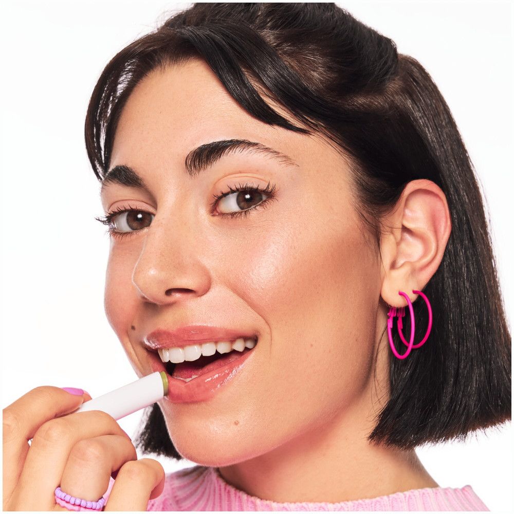 Femme avec du rouge à lèvres. Elle tient un bâton de baume vert.