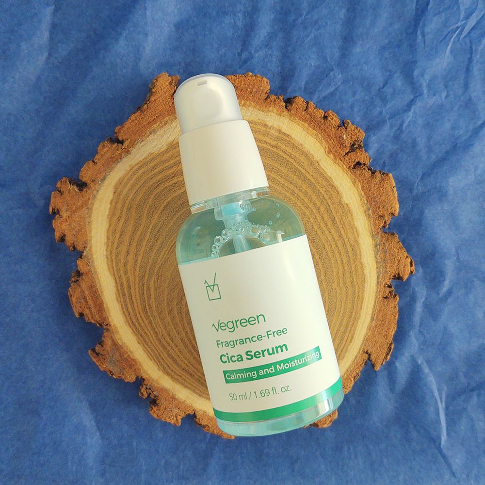 Gezichtsserumfles op houten schijf. Witte pompdop, groene en witte etiketten met tekst. Blauwe vloeistof zichtbaar.