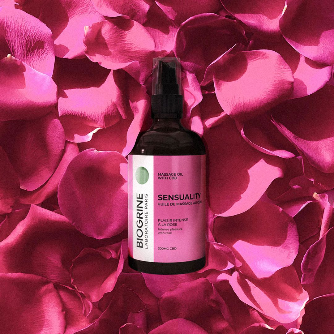 Massageolie fles op rozenblaadjes. Roze etiket met tekst. Merk BIOGRINE.