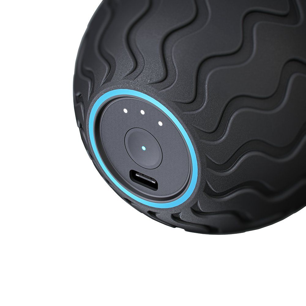 Gros plan sur la balle de massage noire. Panneau de commande avec port de charge, boutons et anneau bleu. Motif ondulé sur la surface.