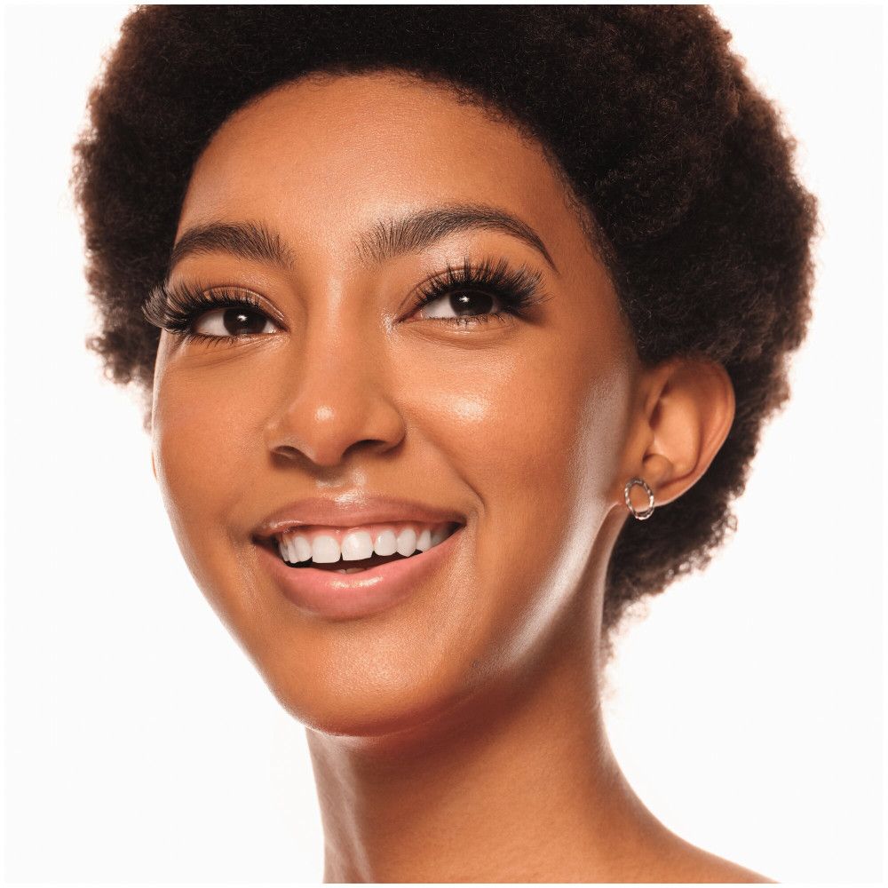 Portrait d'une femme souriante avec des faux cils. Elle a la peau foncée et des boucles courtes.