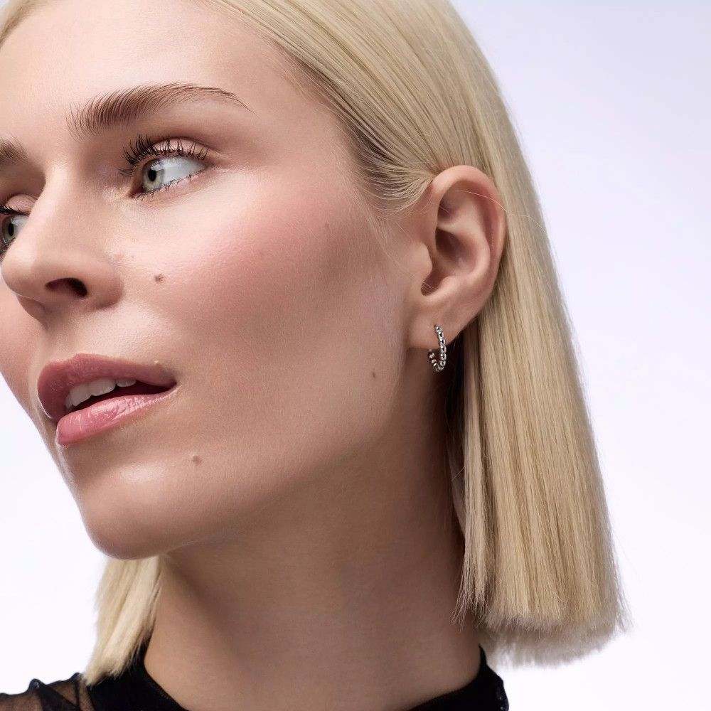 Gros plan d'une femme aux cheveux blonds et aux boucles d'oreilles. Elle regarde sur le côté.