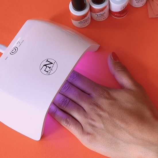 Main dans une lampe à ongles UV. Lampe UV avec logo. Plusieurs flacons de vernis à ongles en arrière-plan.