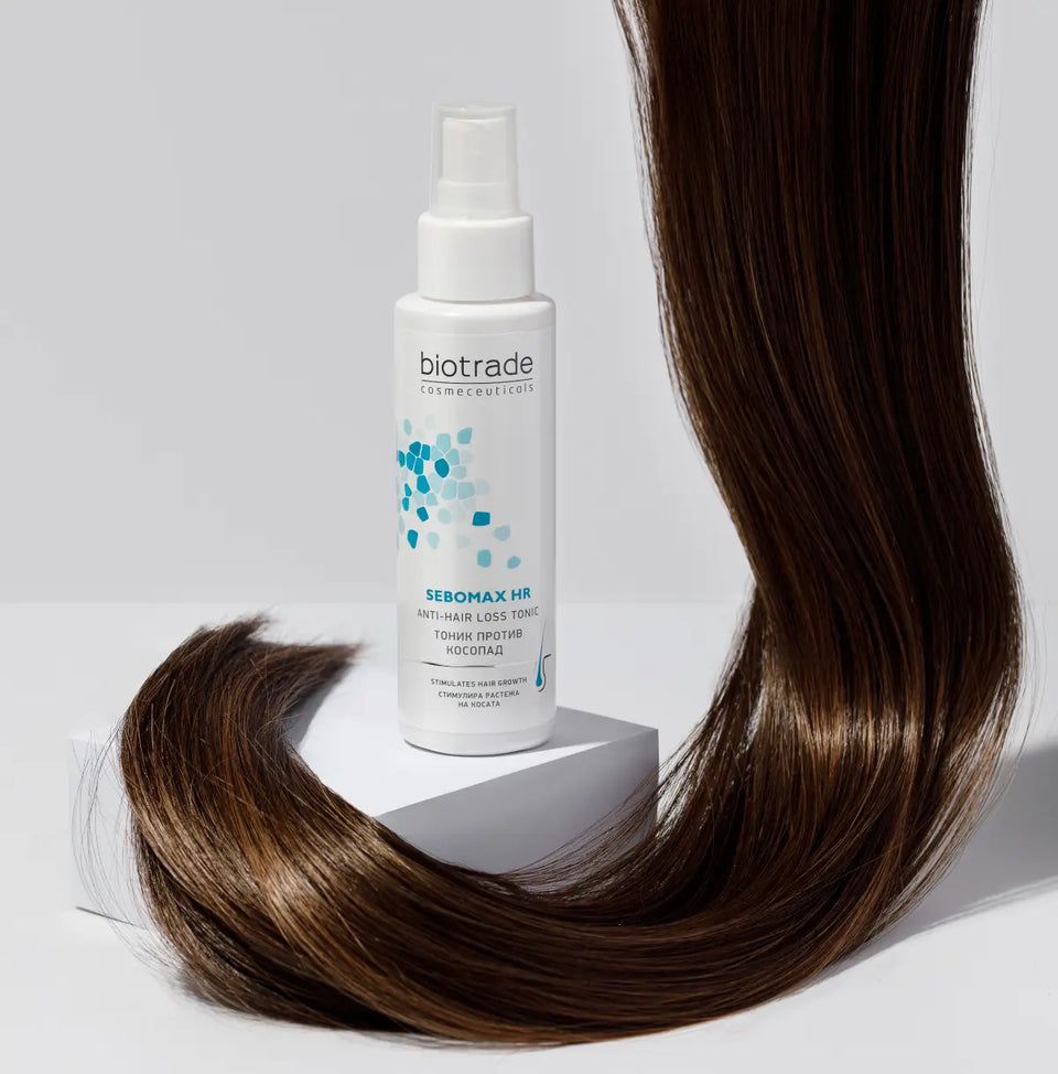 Flacon blanc avec vaporisateur. Logo Biotrade et nom du produit Sebomax HR. Mèche de cheveux à côté.