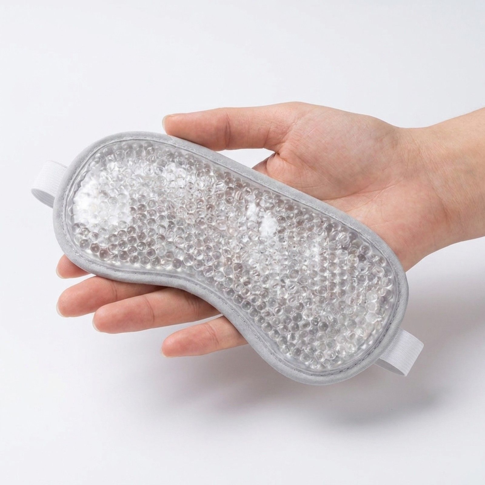 Hand die een grijs oogmasker met parelvulling vasthoudt.