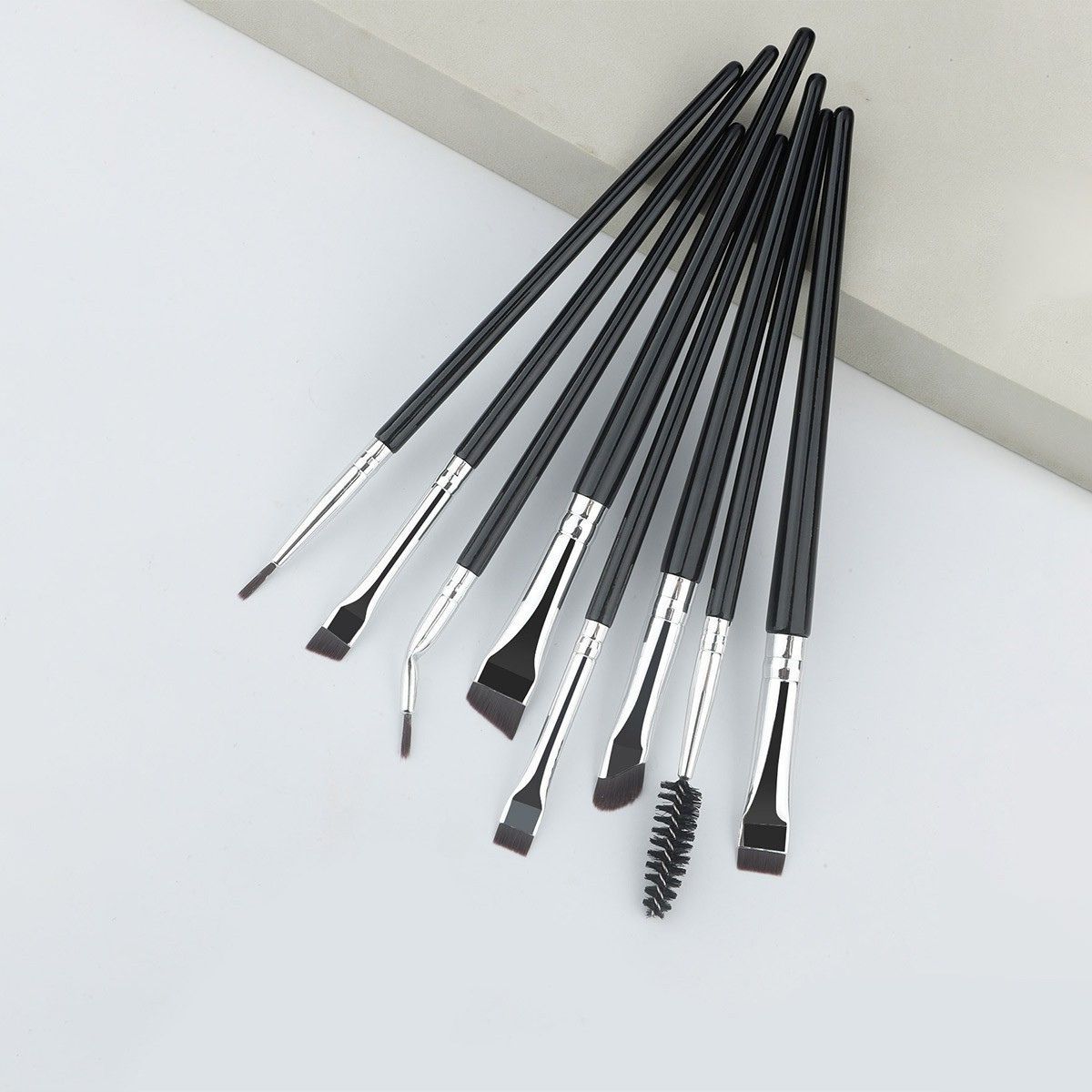 Ensemble de huit pinceaux de maquillage noirs avec viroles argentées et différentes formes de pointe.