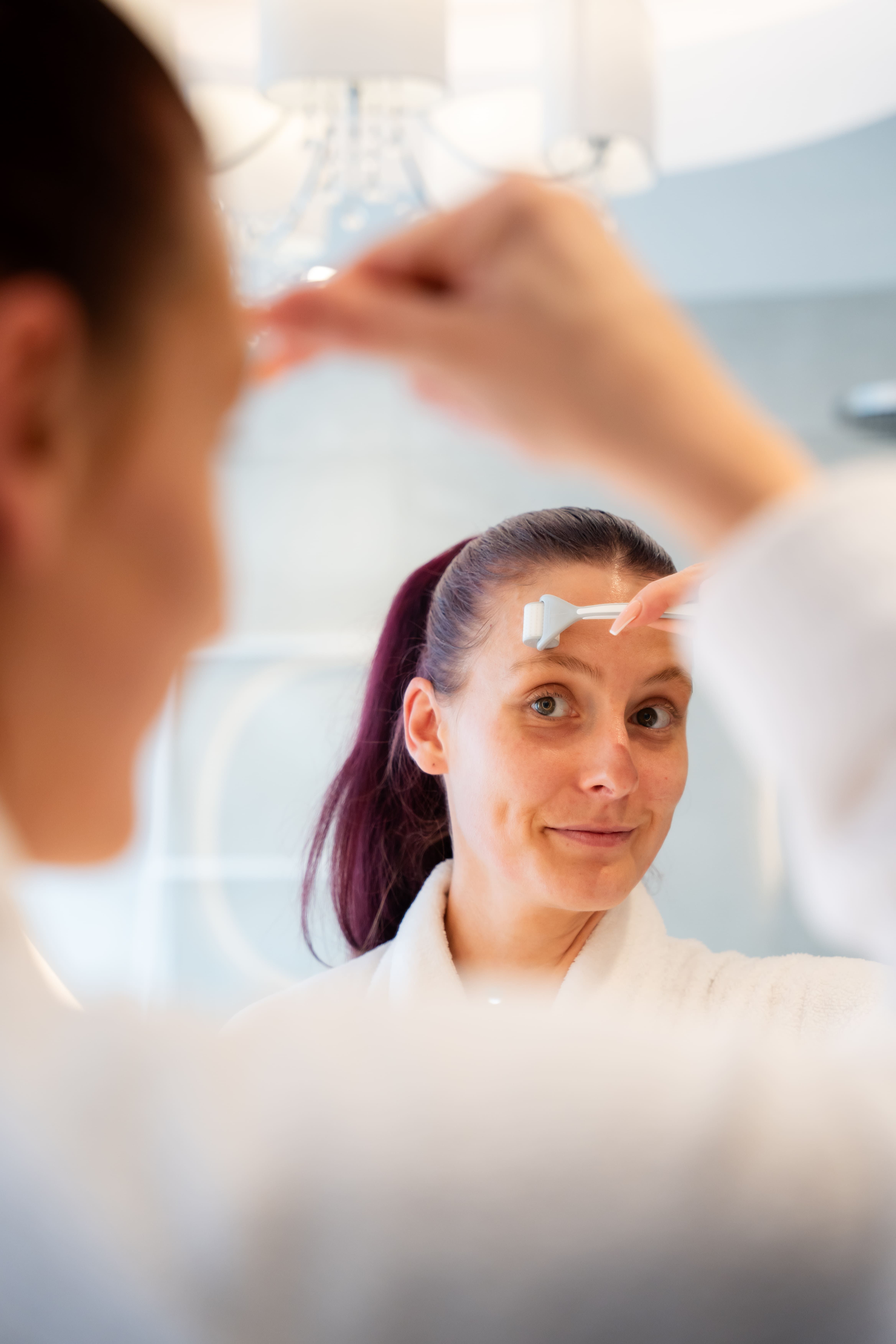 Femme utilisant un dermaroller sur son visage dans un miroir.