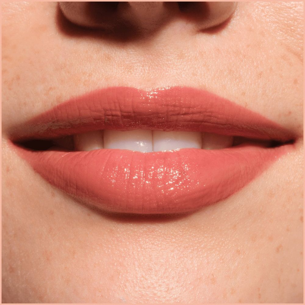 Gros plan sur les lèvres avec un repulpeur de lèvres. Les lèvres sont recouvertes d'un produit rose brillant.