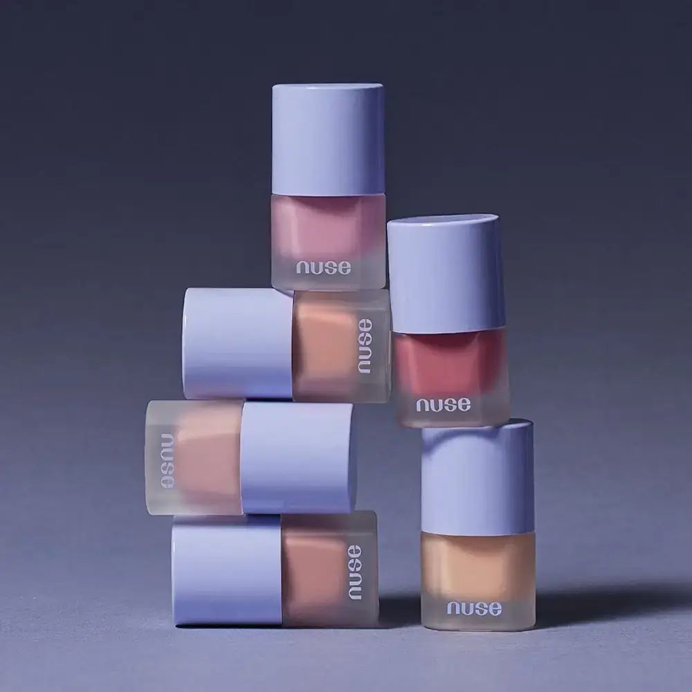 Meerdere flessen vloeibare blush in verschillende tinten. De flessen zijn opgestapeld. De merknaam is op elke fles zichtbaar.