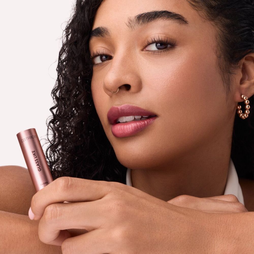 Femme tenant un Gloss Stick rose. Inscription : GLASS LIKE. Elle porte du rouge à lèvres rose.