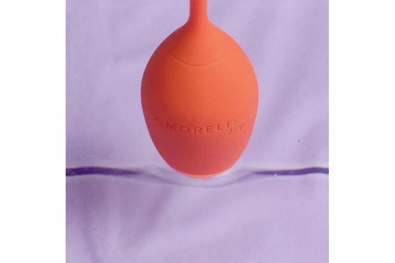 Oranje, eivormig object met de tekst AMORELIE Joy. Het object bevindt zich in een vloeistof.