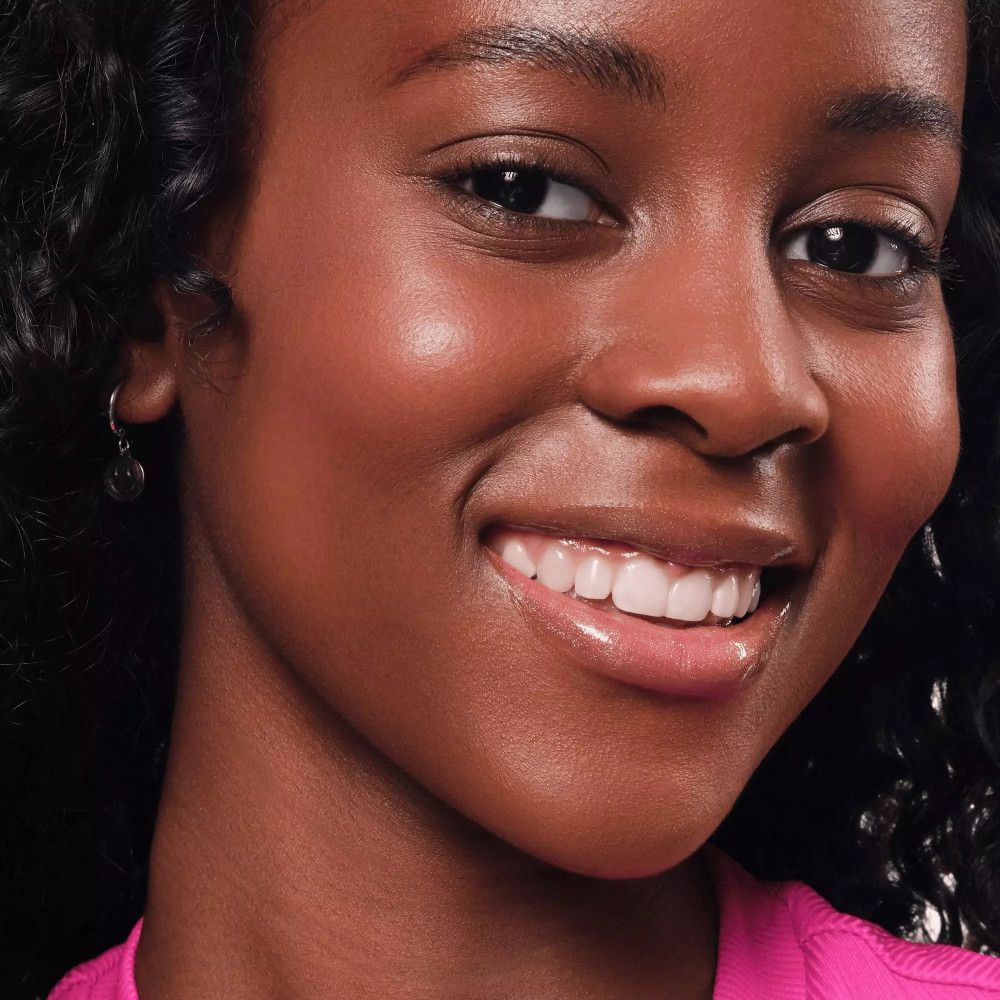 Portret van een vrouw met een donkere huid met Essence Hydra Kiss Lip Oil. Ze glimlacht.