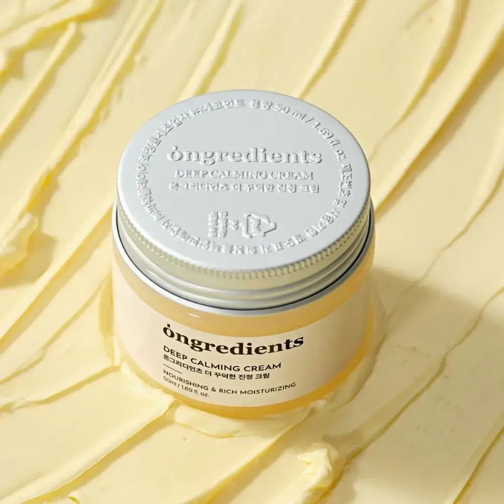 Crèmepot met zilveren deksel. Opschrift: Ongredients, Deep Calming Cream, Koreaanse tekst, Nourishing & Rich Moisturizing. Crème achtergrond.