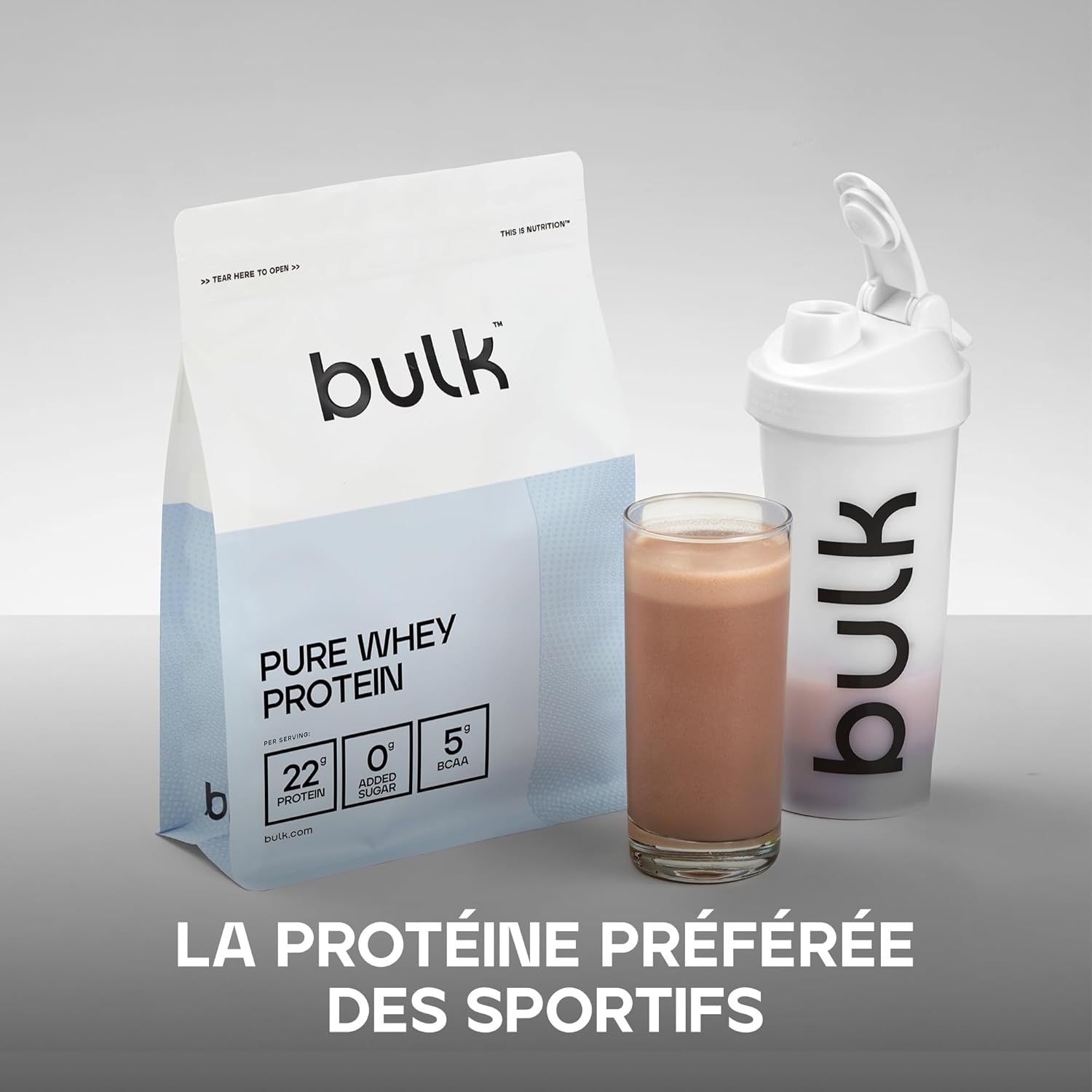 Un paquet de Bulk Pure Whey Protein à côté d'un verre de boisson au chocolat et d'un shaker blanc.