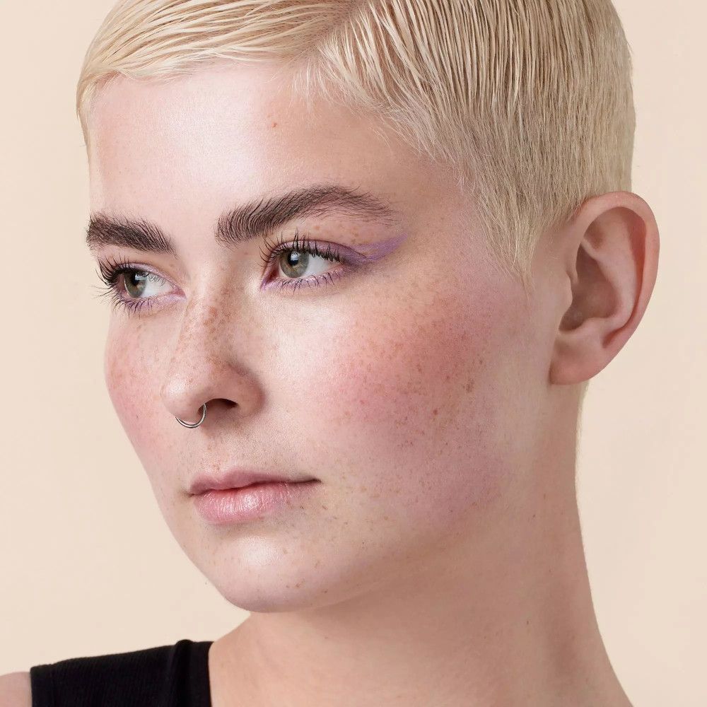 Portret van een vrouw met blond haar en opgemaakte wenkbrauwen. Paarse oogschaduw.