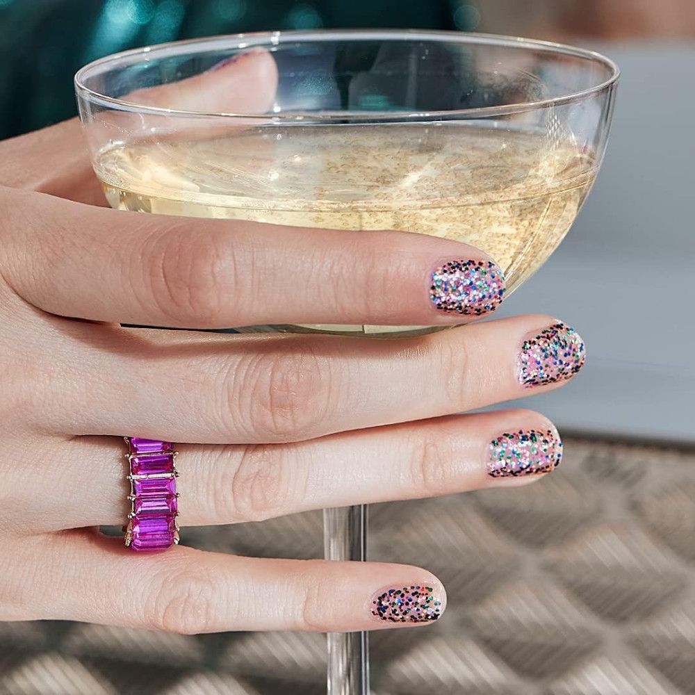 Hand met gelakte nagels die een glas champagne vasthoudt. Nagellak met veelkleurige glitterdeeltjes.