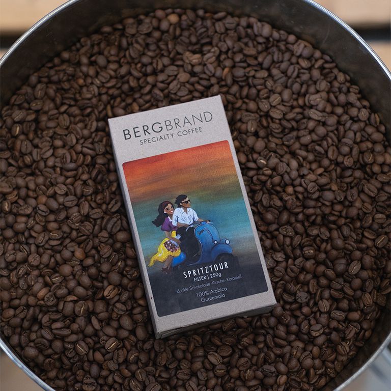Achtergrond van koffiebonen met een doos BERGBRAND Specialty Coffee Spritztour. Doos met scooterillustratie.