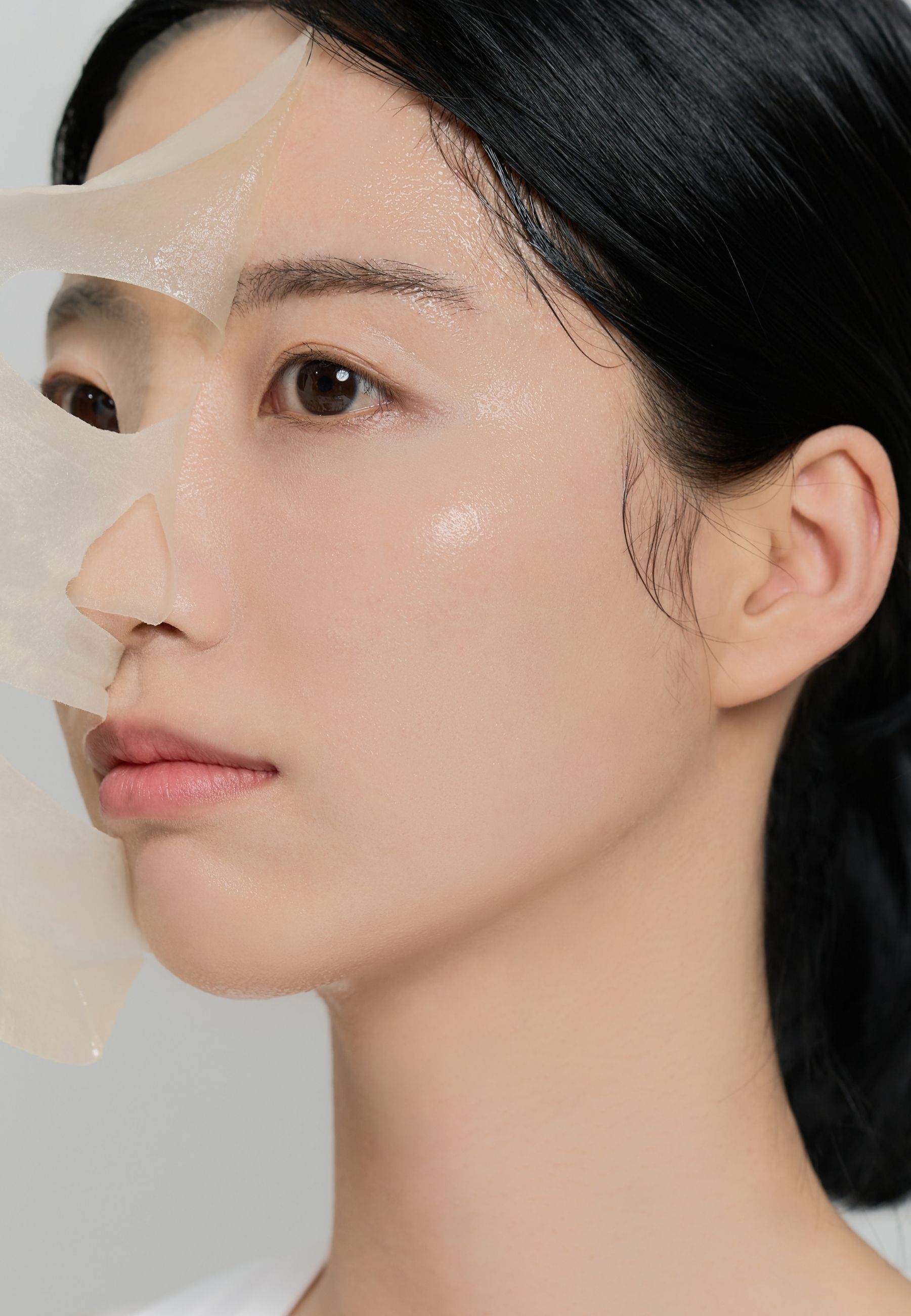 Visage d'une femme avec un masque facial appliqué. Le masque couvre une moitié du visage. La peau brille.