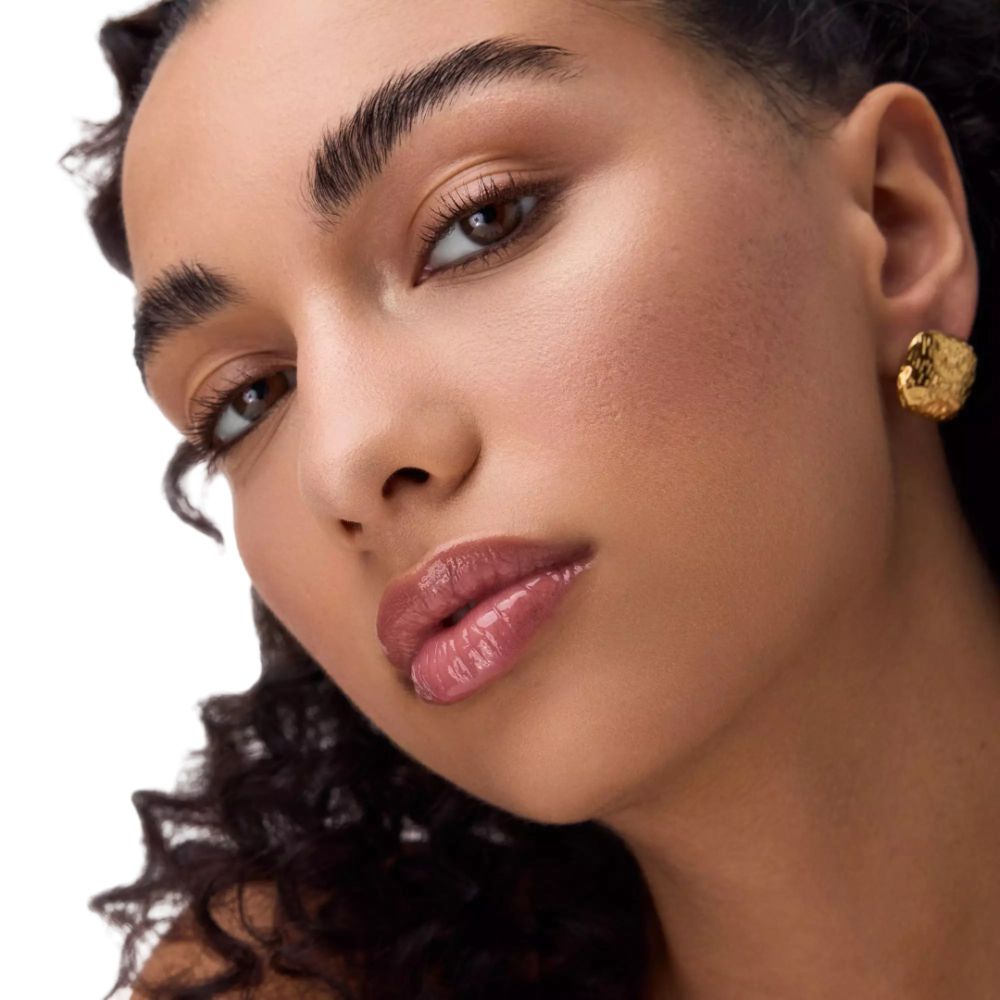 Portret van een vrouw met glanzende lippen. Ze draagt gouden oorbellen.