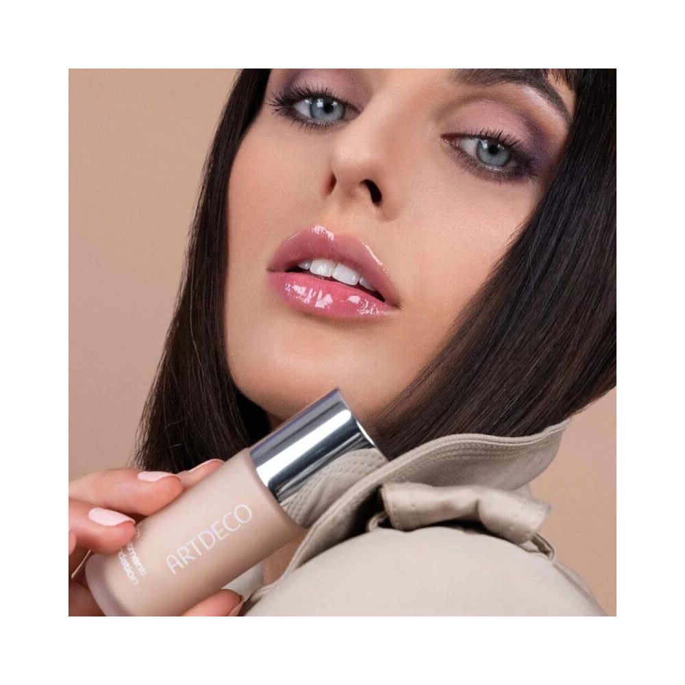 Femme tenant Artdeco Rich Treatment Foundation. Flacon avec bouchon argenté. Nom du produit et marque visibles.