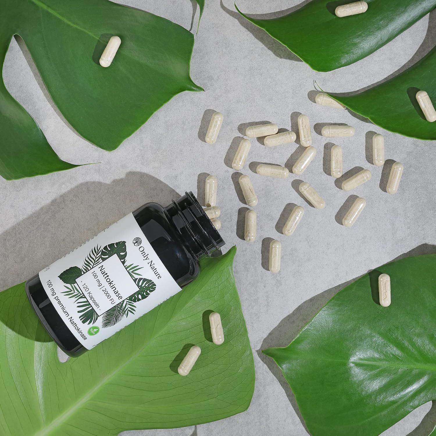 Boîte de gélules Nattokinase avec des feuilles vertes et des gélules éparpillées sur la table.