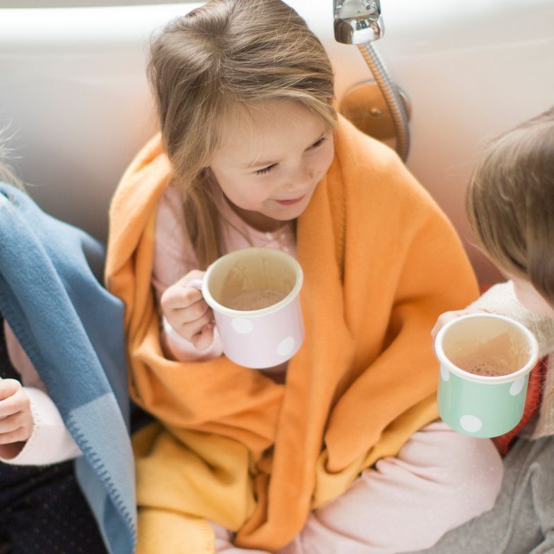Kind met oranje deken en beker. Twee andere kinderen met dekens en bekers. Badkameromgeving.