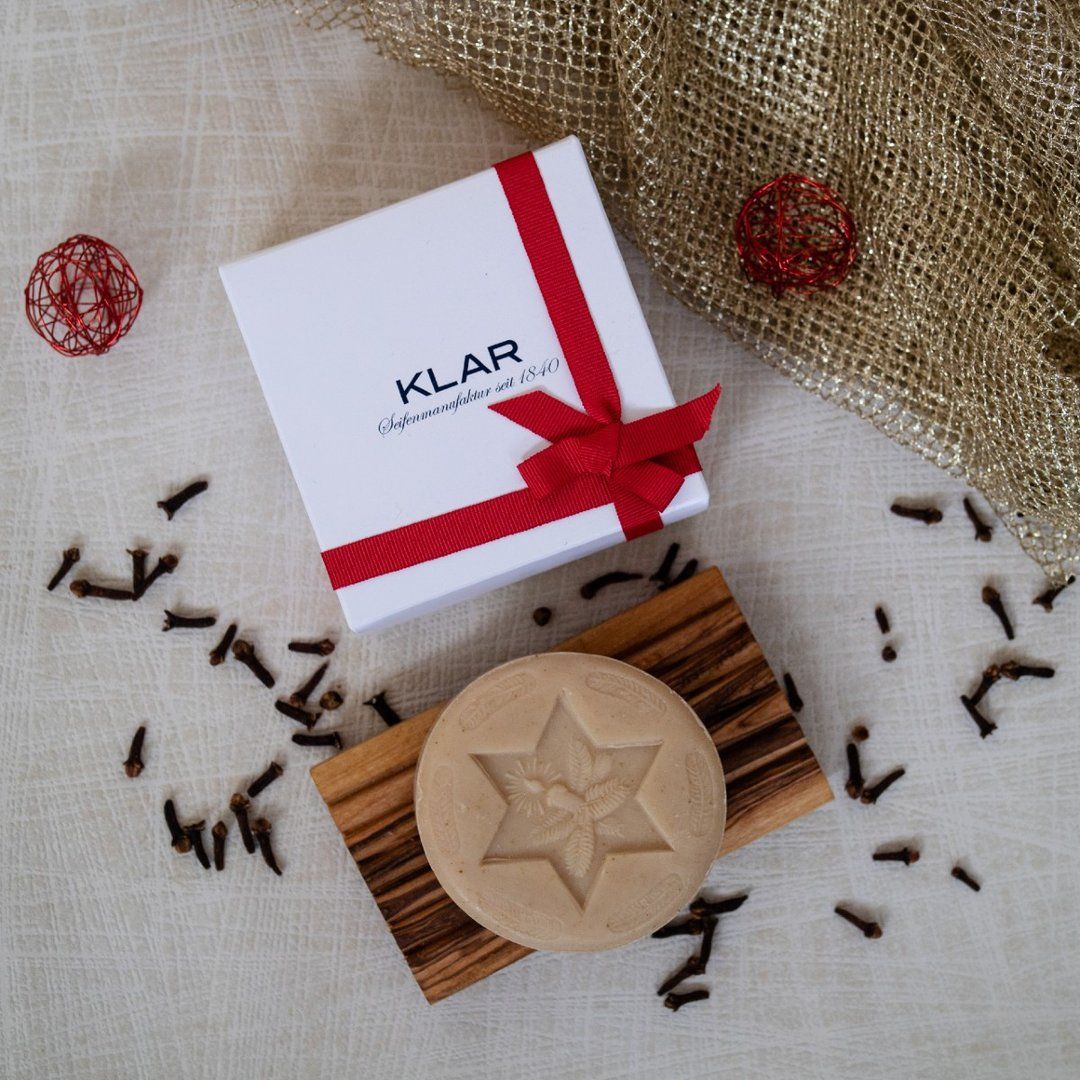 Savon rond avec motif étoile sur porte-savon en bois, coffret cadeau avec ruban rouge, clous de girofle.