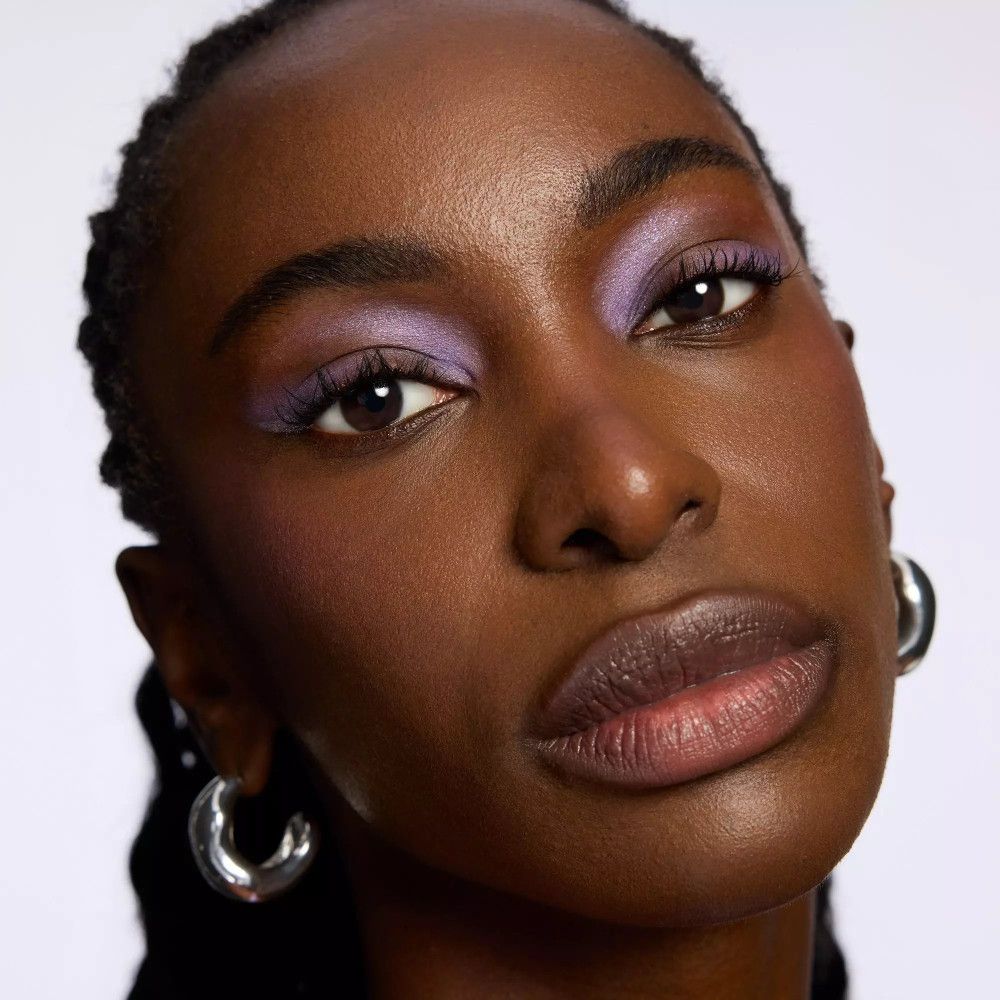 Femme à la peau foncée avec fard à paupières violet. Créoles argentées.