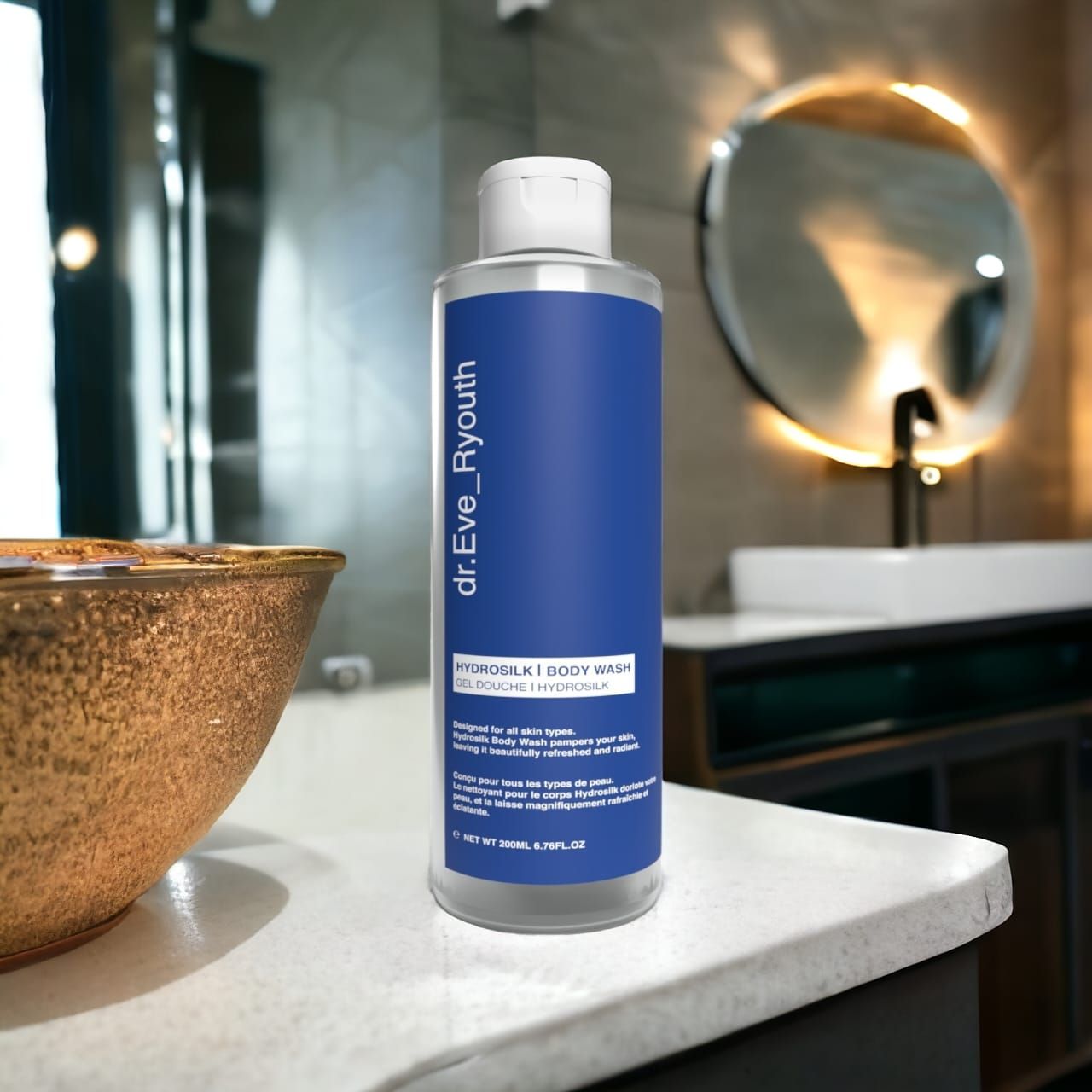 Transparante fles met blauw etiket. Opschrift: dr.Eve_Ryouth, Hydrosilk Body Wash. Badkamer met spiegel en wastafel op de achtergrond.