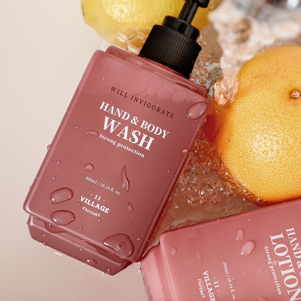 Twee roze hand- en bodywash flessen met water. Tekst: HAND & BODY WASH, Strong protection, 11 VILLAGE FACTORY. Citroenen op de achtergrond.